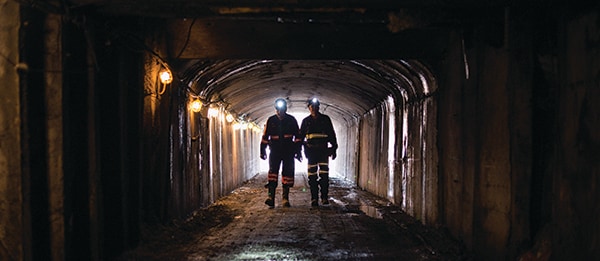 two miners with headlamps on walk down mine entry