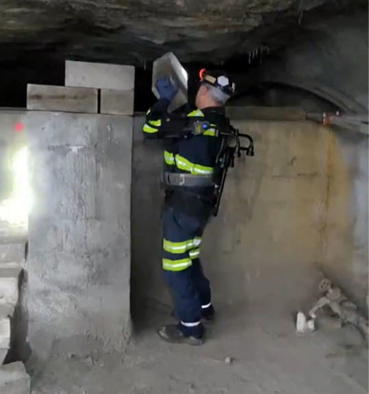 Photo of an exoskeleton being used while a mine worker builds a stopping at an underground research mine.