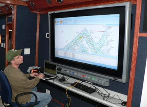 Photo of a command center staff member viewing a situational awareness tool related to mine escape on a large overhead screen.