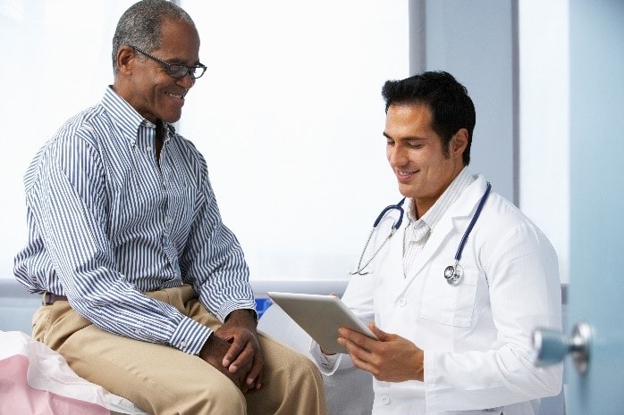 A doctor collects information from a male patient and, using a tablet, enters it into his electronic medical record.