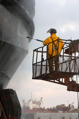 A worker pressure washes a vessel prior to repair.