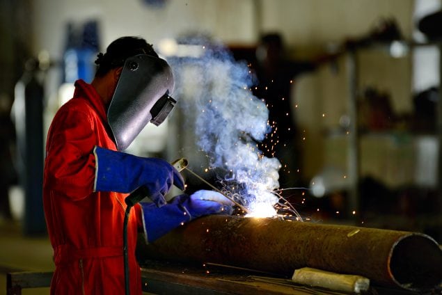 Image of worker wearing personal protective clothing welding a large pipe.