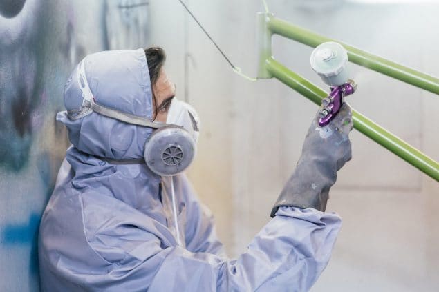 Image of worker wearing personal protective clothing spray painting a bike.