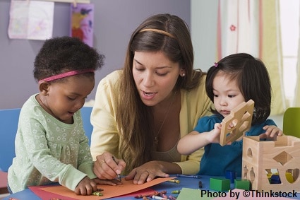 A female preschool teacher helps two girls color and construct with building blocks