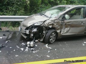 A car damaged from an accident on the side of the road with broken glass, a smashed driver side door and fender