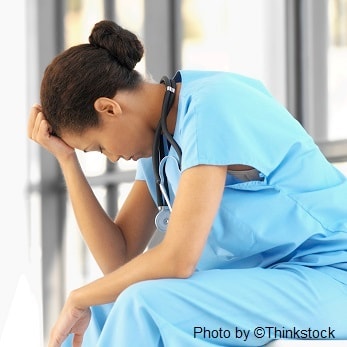 A nurse sits with her hand on her forehead