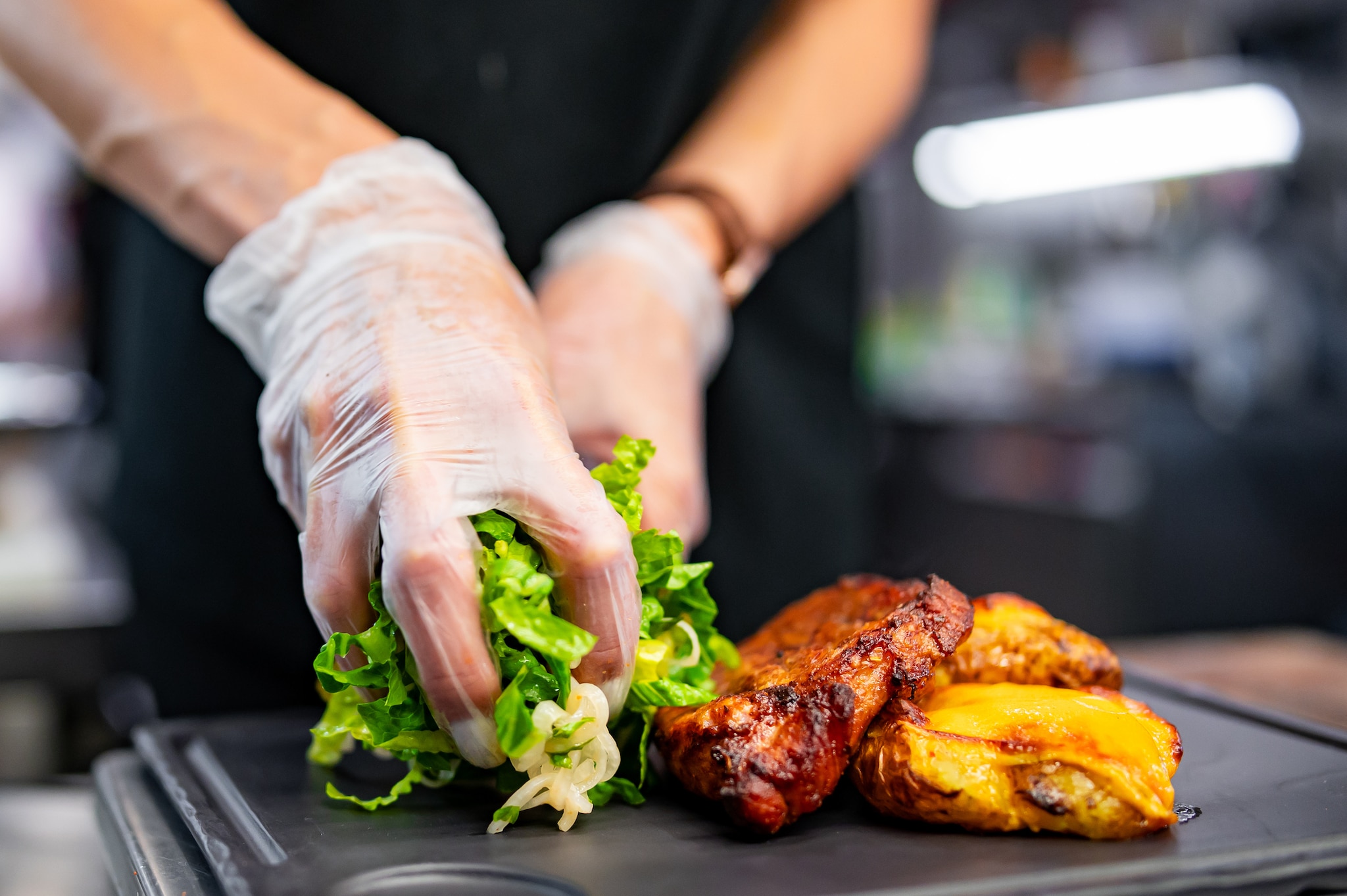 Restaurant chef with gloved hands placing salad and meat on plate.