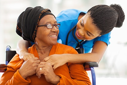 older woman with headwrap embraced from behind by younger medical professional
