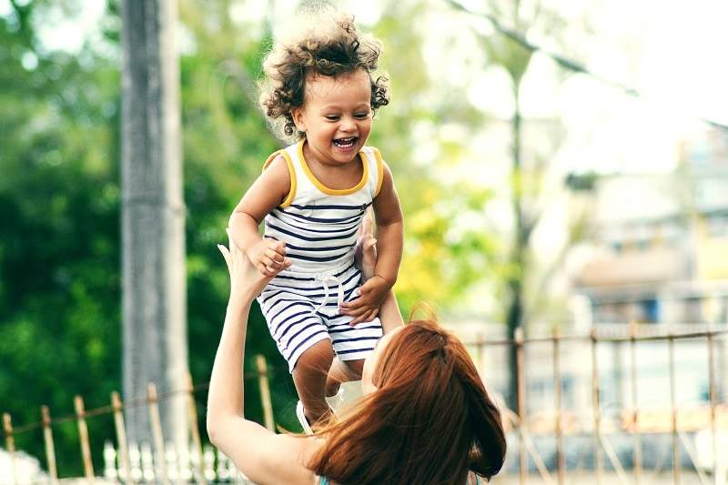 Woman lifting smiling child overhead. Child is wearing outfit with stripes.