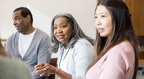Black man, Black older woman, and Asian woman participating at a conference table.