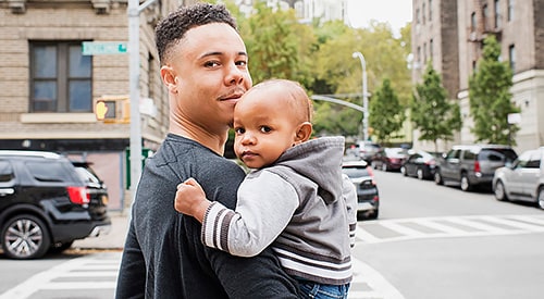 Young college-aged black man holding a toddler in downtown area.