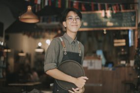 Teenage boy waiter looking at camera smiling work at cafe opening