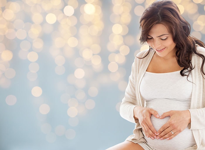 mujer embarazada haciendo gesto de corazón en su estómago