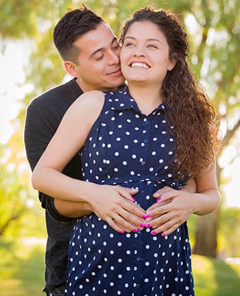 Hombre hispano abraza a su esposa embarazada aire libre en el parque