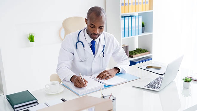 A clinician sitting at a desk referring to some reference documents.