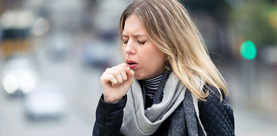 Woman coughing, standing in a city street