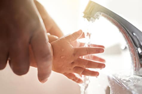 Adult helping a child wash their hands.