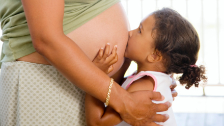 Niña besando el vientre de su mamá embarazada