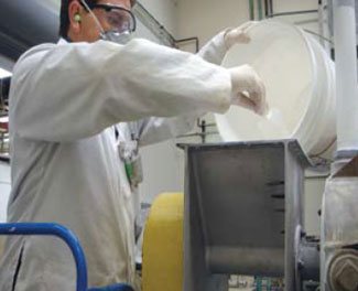 Un trabajador que labora en la producci&oacute;n de nanopart&iacute;culas viste un equipo de protecci&oacute;n d&eacute;rmico, respiratorio y auditivo y un aparato de muestreo personal de aire durante una operaci&oacute;n de vertimiento.
