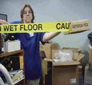 Persona sosteniendo cinta adhesiva amarilla de aviso de que el piso está mojado