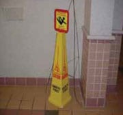 Señal de piso mojado amarilla en forma de cono con una señal de advertencia pues-ta en la parte de arriba