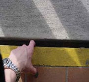 Persona con el dedo apuntando hacia abajo a una separación grande entre las baldosas de un pasillo exterior