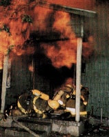 Bomberos usando aparatos de respiración autónomos (SCBAs, por sus siglas en inglés) y otros equipos de protección en el lugar de un incendio. 
