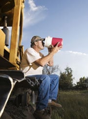 Hombre sentado al borde de un tractor bebiendo de una grande jarra de agua