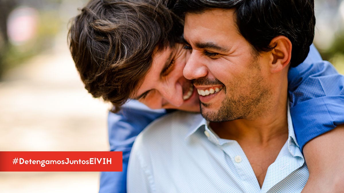 Comenzar el tratamiento es el paso más importante después del diagnóstico del #VIH. Puedes mantenerte saludable si lo empiezas lo más pronto posible. Aprende más: https://bit.ly/2ZqGYXT #DetengamosJuntosElVIH - Two men smiling with one hugging the other from behind