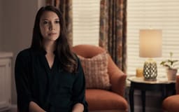 White female sitting in room with window and chair behind her talking to camera