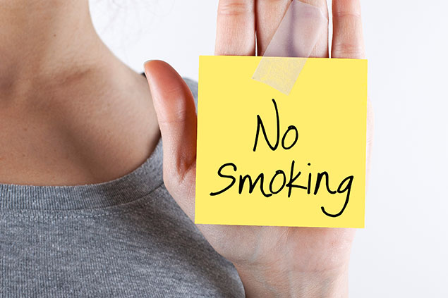 Woman holding a post-it note with No Smoking written on it.
