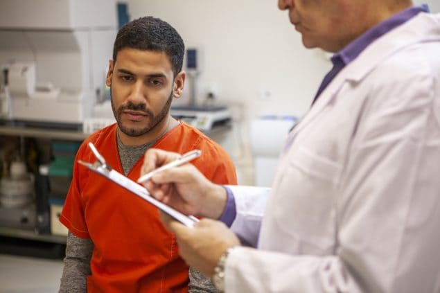 Male doctor providing medical attention to Latin American male prison inmate in correctional medical facility