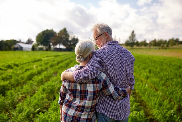 An older couple embracing each other while standing on a rural farm