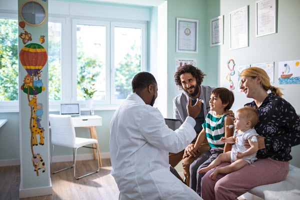 Médico afroamericano hablando a una familia blanca con un niño pequeño y un bebé.