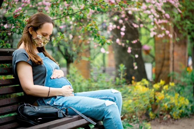 Mujer embarazada sentada en un banco mirándose el vientre y sosteniéndolo con las manos