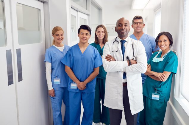 Diverse group of healthcare staff standing in a white hallway.