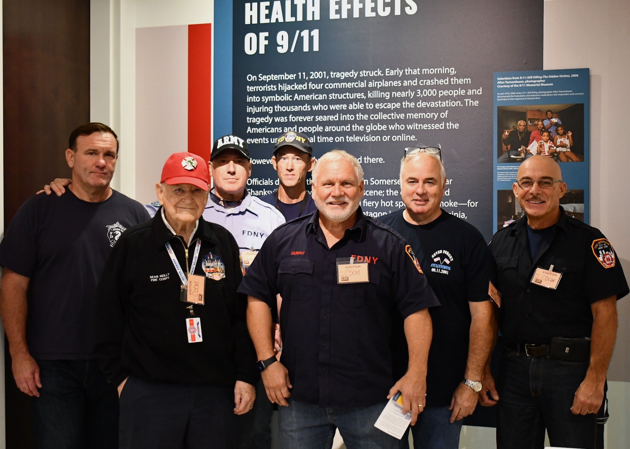 Tim Murphy, retired NYC firefighter and WTC Health Program member, stands proudly with a group of fellow 9/11 responders who are members of the NYC Shields of Georgia, a organization founded by Tim. The joyous group is captured with smiles during a memorable moment at the Health Effects of 9/11 exhibition at the CDC museum, embodying strength, camaraderie, and resilience. 