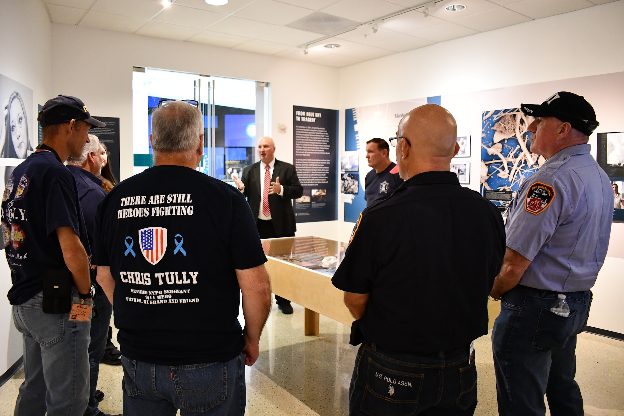 The NYC Shields of Georgia, a group of 9/11 responders led by retired NYC firefighter Tim Murphy, gathered around an exhibition piece at the Health Effects of 9/11 exhibition in the CDC museum. In a moment of solidarity, they listen intently to a speaker, embodying the shared support that defines their mission. 