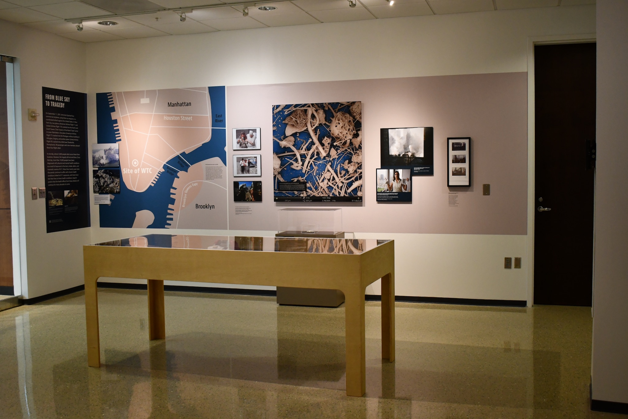 A wall displaying a map, images of 9/11 survivors and responders, and a microscopic view of dust from the Health Effects of 9/11 Exhbition.