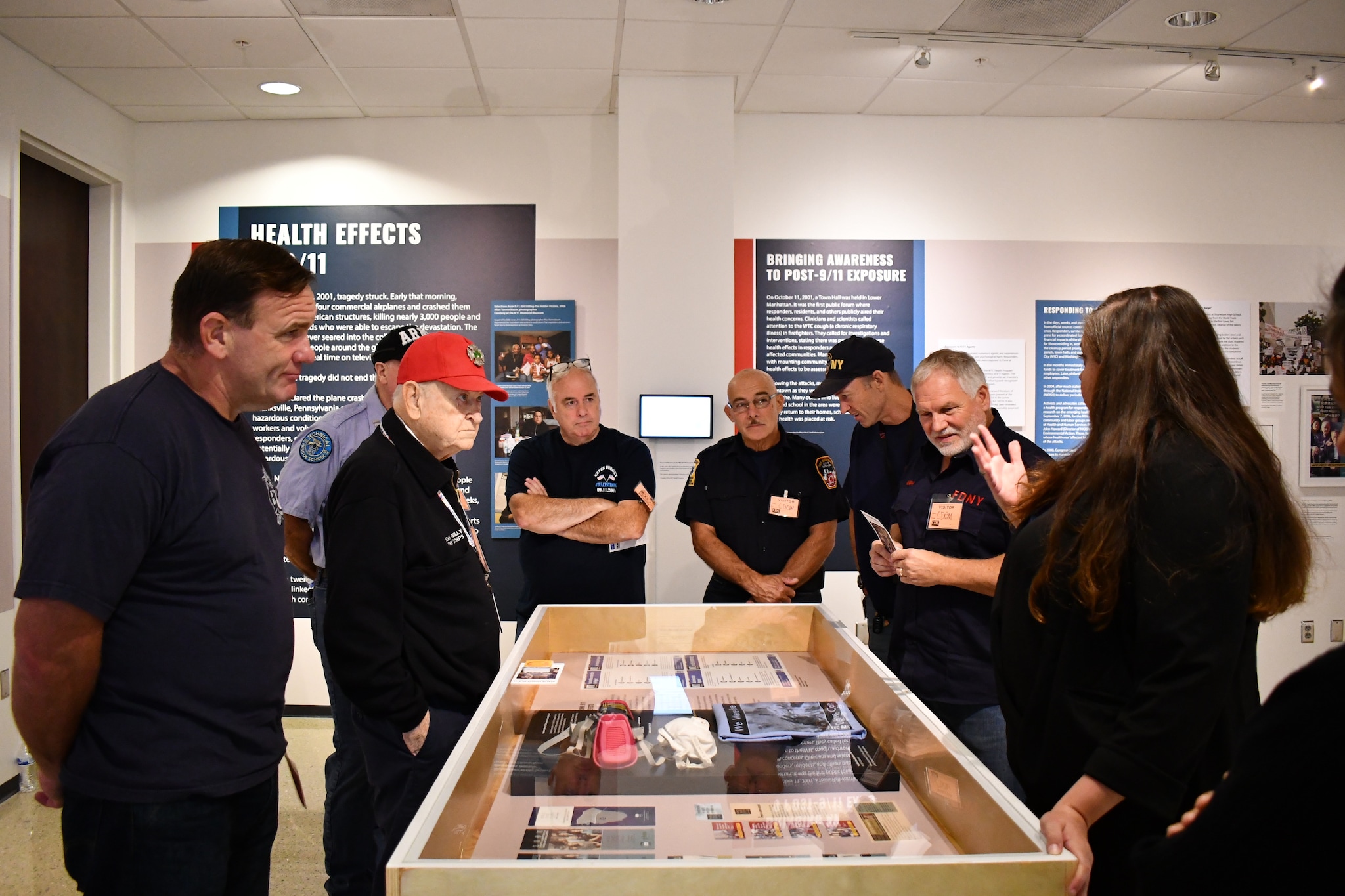 Tim Murphy and a group of fellow responders stand around a glass display case discussing the exhibit at the Health Effects of 9/11 Exhibition.