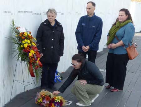 VCF Special Master Allison Turkel accompanied by 3 other WTC Health Program Staff paying tribute, solemnly looking over an arrangement of flowers placed against the Memorial Wall of victims' names at the Flight 93 National Memorial in Shanksville. The photo is heartfelt homage, capturing a moment of reflection, remembrance and community.