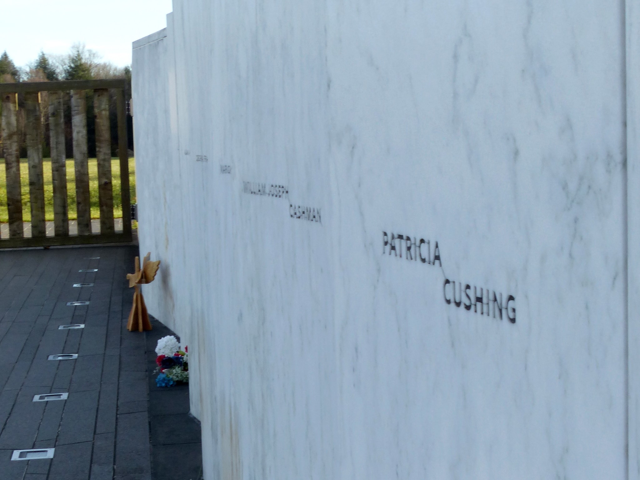 A memorial wall with victim names at the Flight 93 National Memorial. Flowers are placed on the ground in front of it.