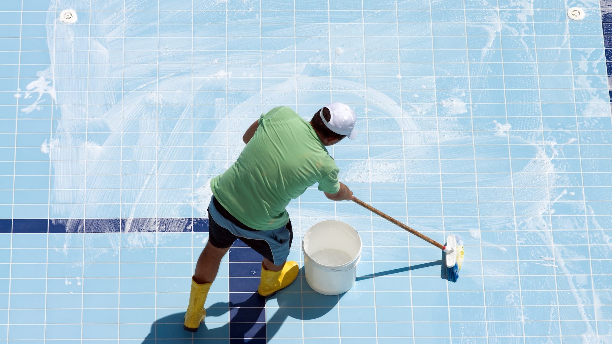 Man cleaning bottom of an empty pool with a bucket and mop.