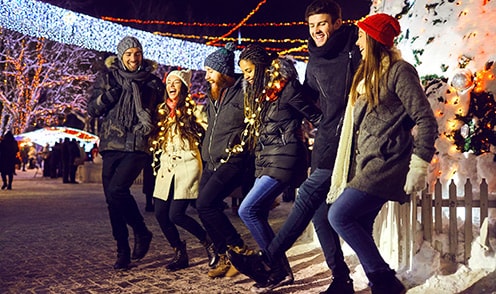 A group of friends walking outside in the snow and holiday lights.