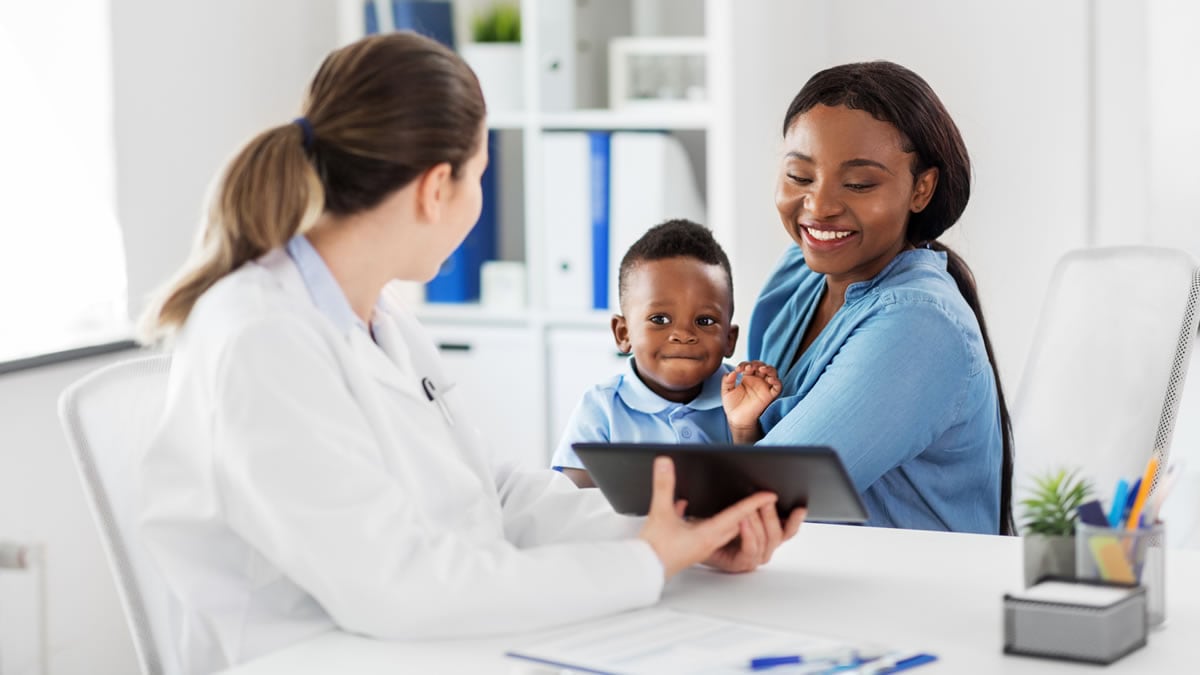 A healthcare professional consults with a smiling patient and child
