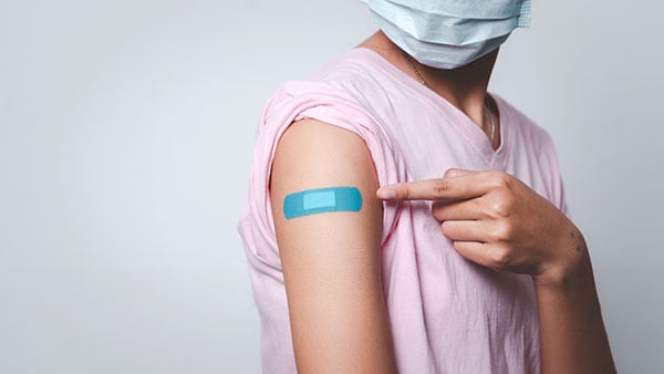 Young woman pointing to an adhesive bandage on her arm after injection of vaccine