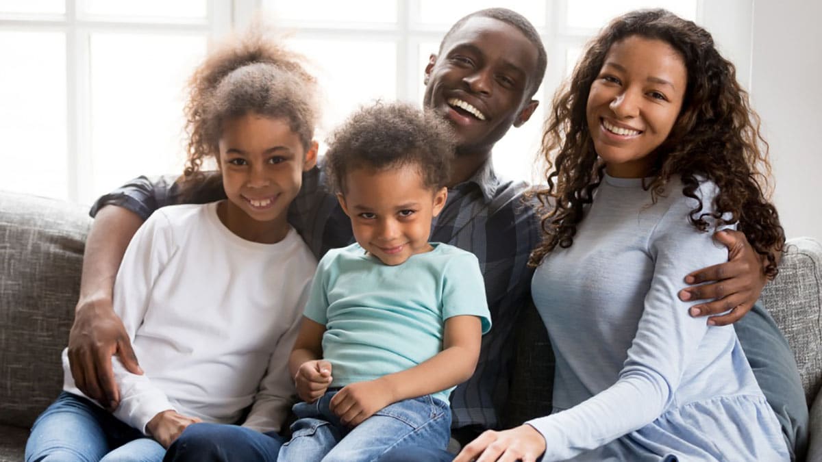 An African American family with two adults and two kids sitting on couch.