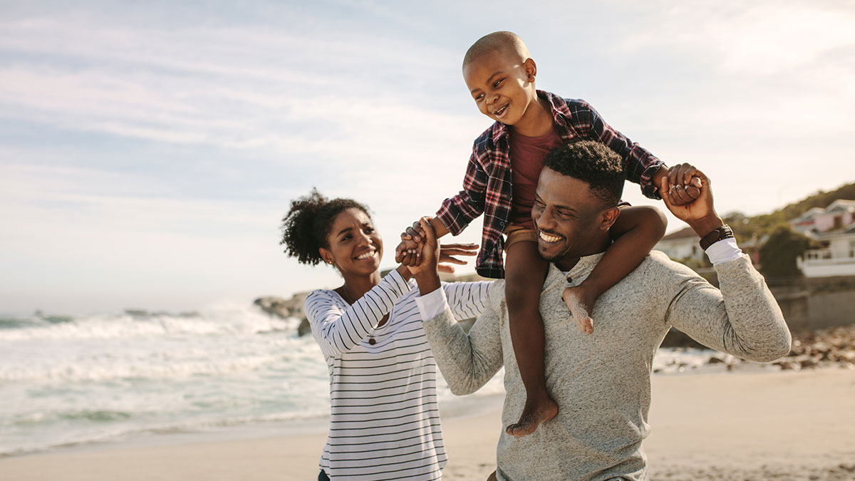 African American family walking on beach. Dad carrying son on shoulders.