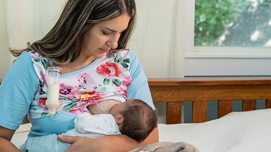 Mother breastfeeding her baby using a supplemental nursing system.