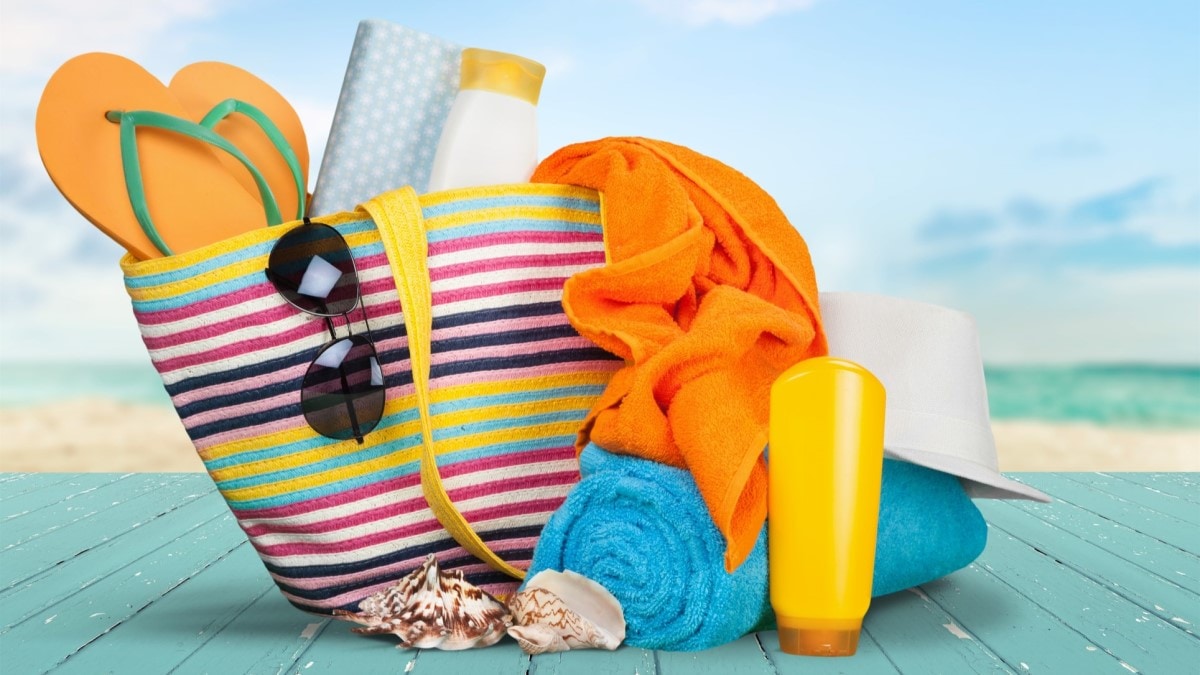 Photo of a colorful tote bag containing sunscreen, sunglasses, a hat, towels, and shoes